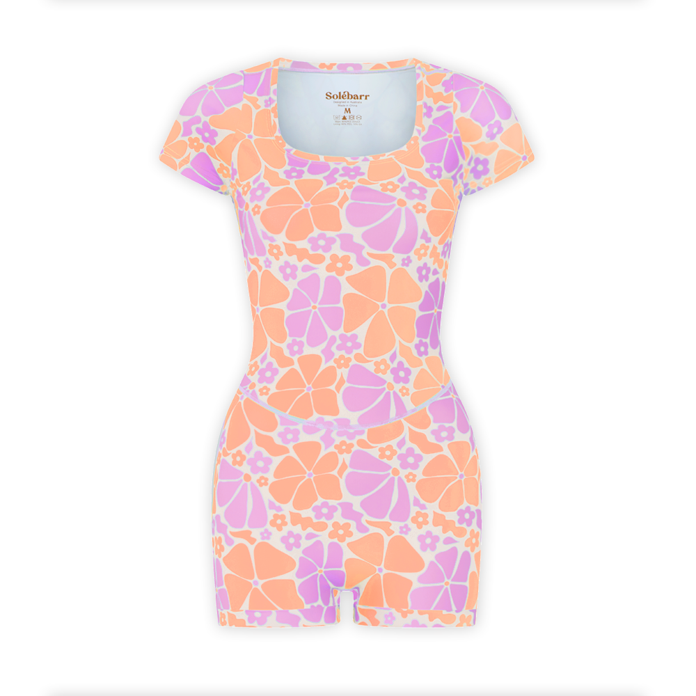 A shortie suit with a floral pattern in shades of pink, orange, and purple, featuring short sleeves and boyleg design.